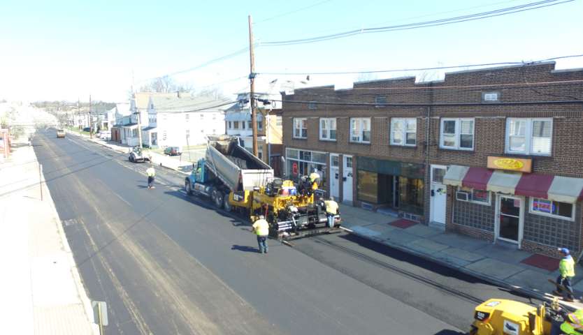 Aerial shot of workers and machinery paving an urban street lined with buildings.