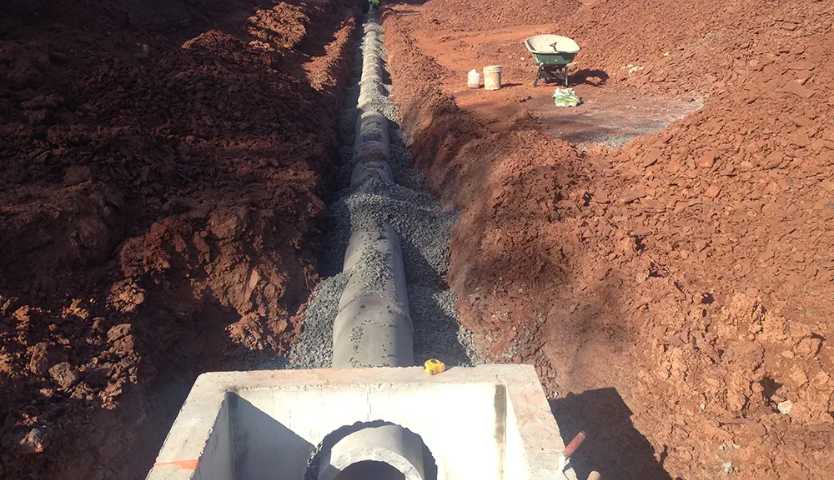 Deep trench showing large pipeline installation amid reddish soil.