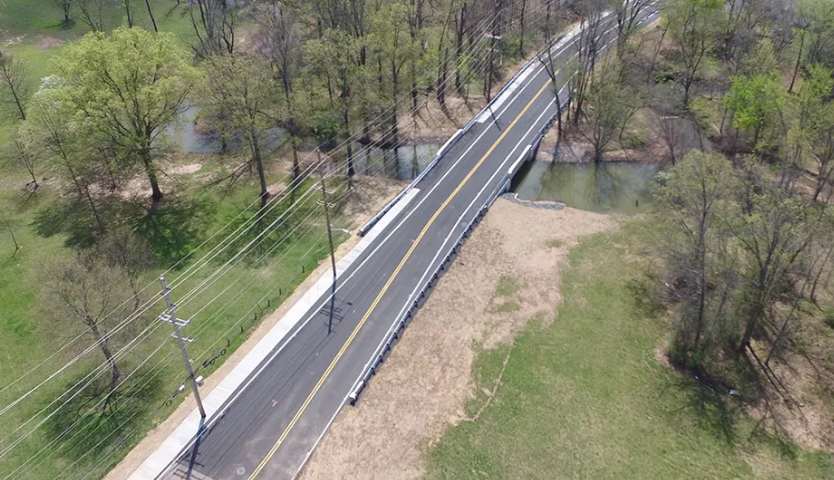 Aerial view of a paved road cutting through trees and crossing a stream.